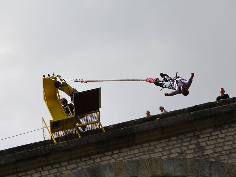 Homme effectuant un saut à l'élastique depuis une plateforme sur un viaduc, avec des spectateurs en arrière-plan.