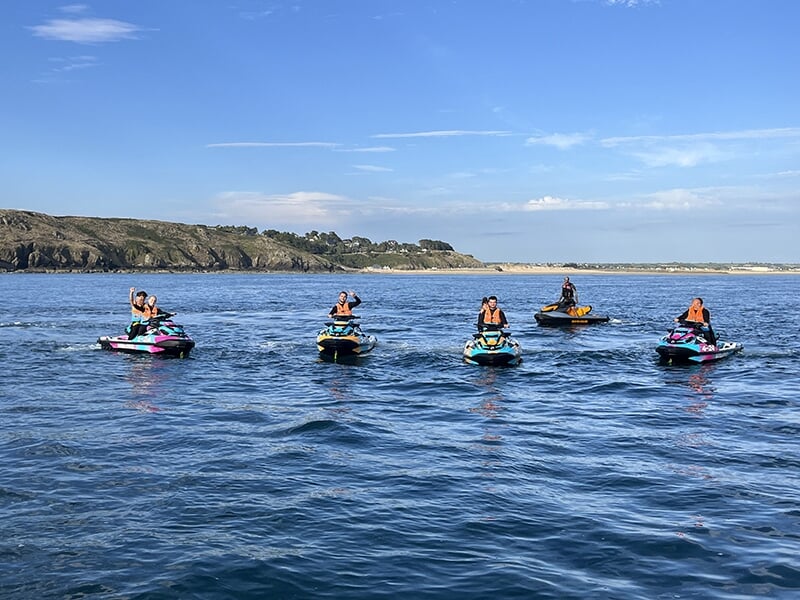 Un groupe de cinq motomarines alignées sur l’eau, avec un arrière-plan de côte rocheuse sous un ciel bleu clair.