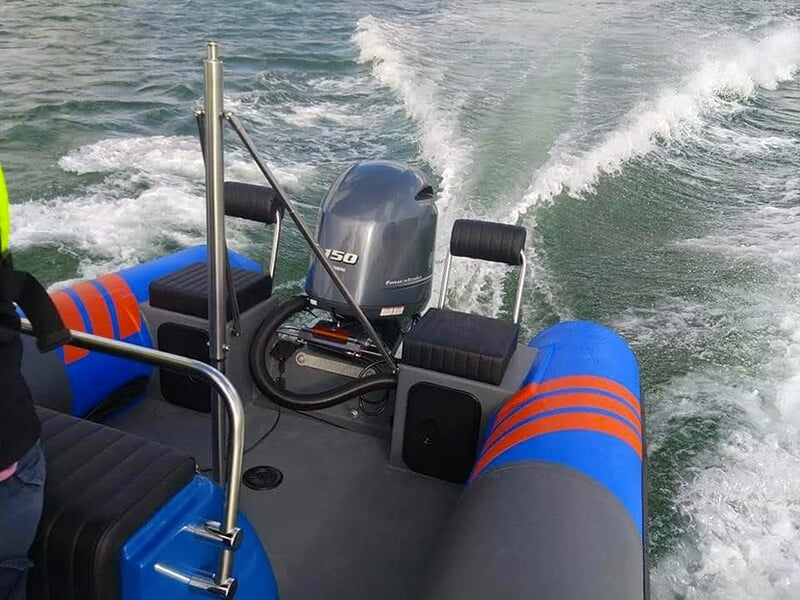 Vue arrière d'un bateau pneumatique avec un moteur hors-bord de 150 chevaux, laissant une traînée dans l'eau calme pendant la navigation.