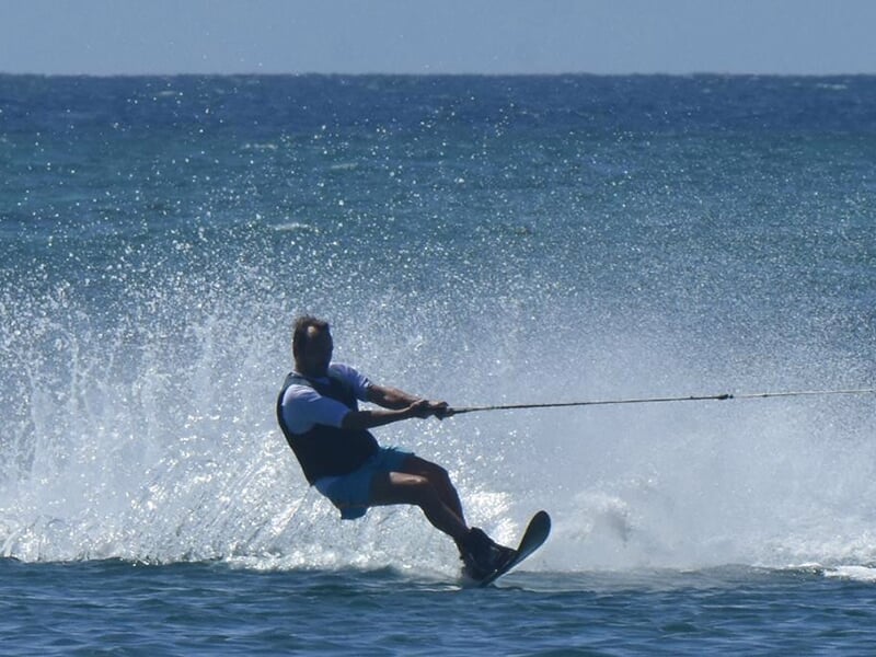 Une personne pratiquant le ski nautique, s'appuyant sur un seul ski, avec des éclaboussures d'eau derrière lui et un horizon dégagé.