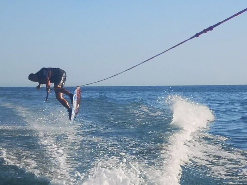 Un wakeboarder en pleine figure aérienne, tenant une corde, sur une mer calme sous un ciel dégagé.