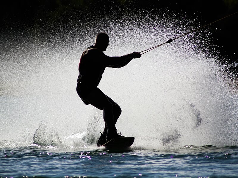 Silhouette d'un wakeboarder glissant sur l'eau, entouré d'éclaboussures et capturé en contre-jour.