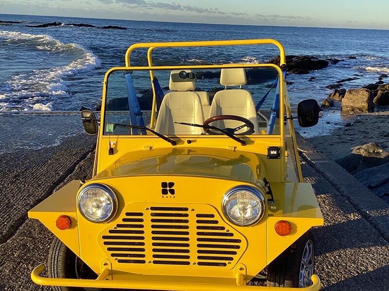 Vue avant de la voiture jaune décapotable garée sur une rampe près de l’océan, avec des sièges blancs et un volant en bois.
