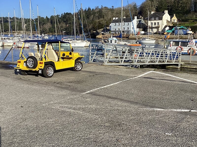 Vue latérale d’une voiture jaune décapotable garée près d’un port de plaisance.