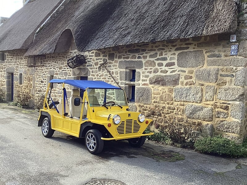 Voiture jaune décapotable stationnée devant une maison en pierre avec un toit de chaume.