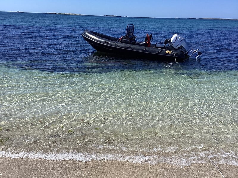 Un bateau pneumatique noir amarré dans une eau cristalline près d'une plage de sable blanc.