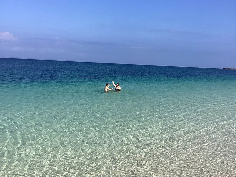 Deux personnes nageant dans une mer turquoise et limpide sous un ciel bleu dégagé.