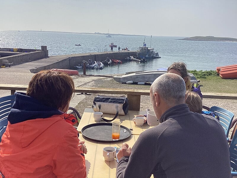 Un groupe de personnes assises à une table en plein air avec vue sur un port et la mer à l'horizon.