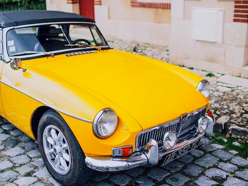 Avant d'une MGB décapotable jaune vif garée sur un sol pavé.