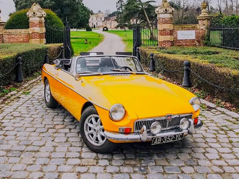 MGB décapotable jaune vif devant une grande allée menant à un château.