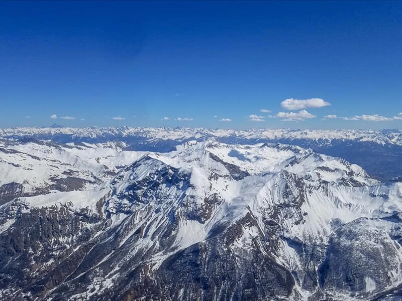 Vue aérienne spectaculaire des sommets enneigés des montagnes sous un ciel bleu vif, prise depuis un avion.