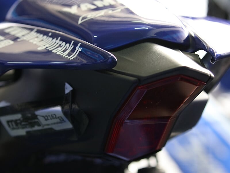 Vue rapprochée de l'arrière d'une moto Yamaha, mettant en évidence le feu arrière rouge et la finition bleue brillante avec des détails de sponsor.