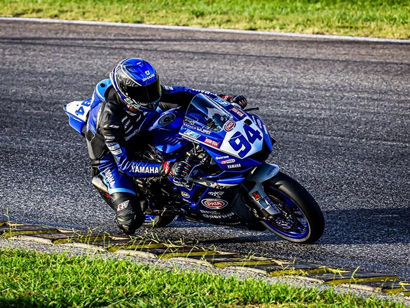 Motard sur une Yamaha bleue n°94 en pleine courbe, incliné pour négocier un virage serré sur piste.