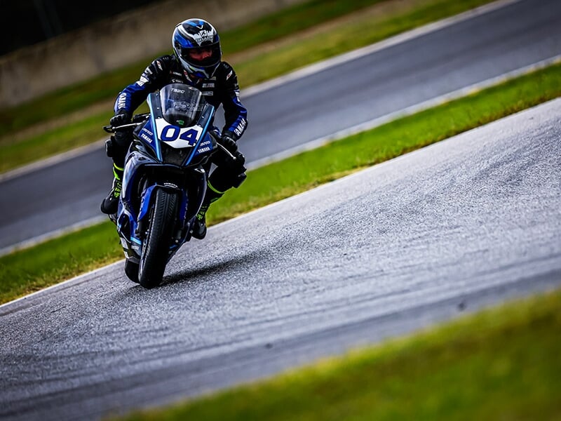 Vue frontale d'un motard sur une Yamaha n°04, roulant sur une piste avec de l'herbe des deux côtés.