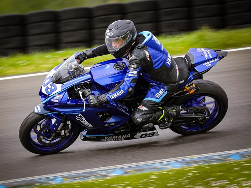 Vue latérale rapprochée d’un motard sur une Yamaha bleue n°03 sur une piste de course.