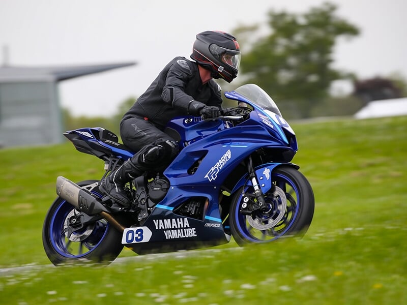 Motard sur une Yamaha bleue n°03 roulant sur une piste entourée de verdure.