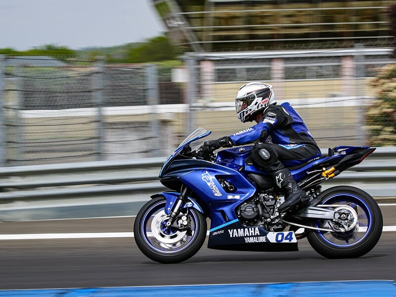 Vue latérale d'un motard sur une Yamaha bleue n°04 roulant rapidement sur une piste entourée de barrières.