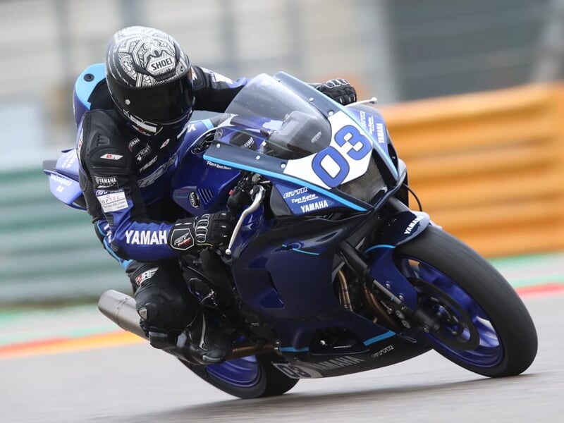 Pilote en combinaison bleue et casque intégral noir et blanc sur une moto Yamaha bleue numéro 03 en virage sur circuit