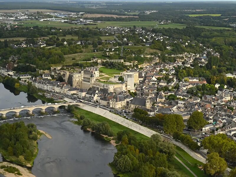 Vue aérienne d'une ville pittoresque avec un pont traversant une rivière et un château au centre entouré de verdure.