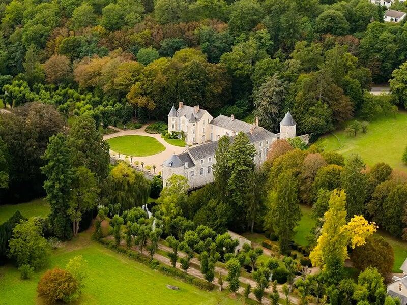 Château historique situé dans un domaine boisé avec des jardins soignés et une architecture classique.