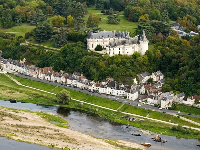 Château perché sur une colline surplombant une rivière et un village charmant avec des maisons alignées le long de la berge.