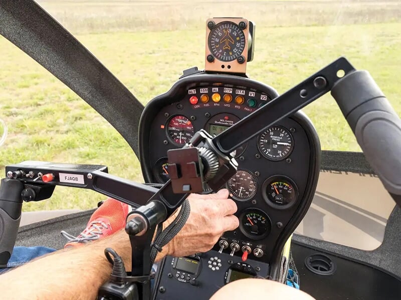 Vue rapprochée de l'intérieur d'un cockpit d'hélicoptère avec des instruments de navigation et les mains d'un pilote ajustant les commandes.