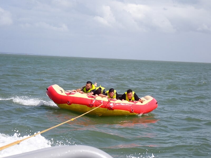 Groupe de quatre personnes allongées sur une bouée gonflable rouge, tirée sur l'eau calme.