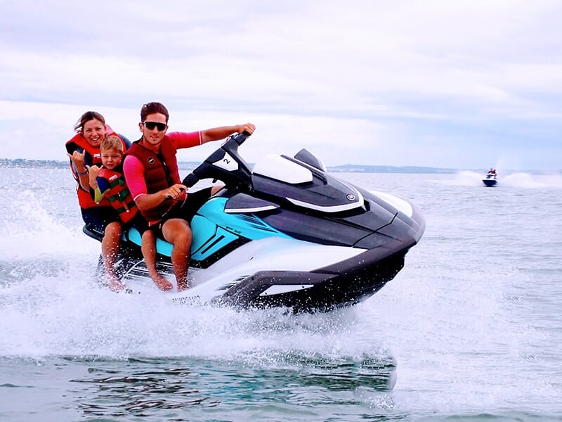 Famille de trois personnes, un homme, une femme et un enfant, profitant d'un tour en jet-ski sur une mer calme.