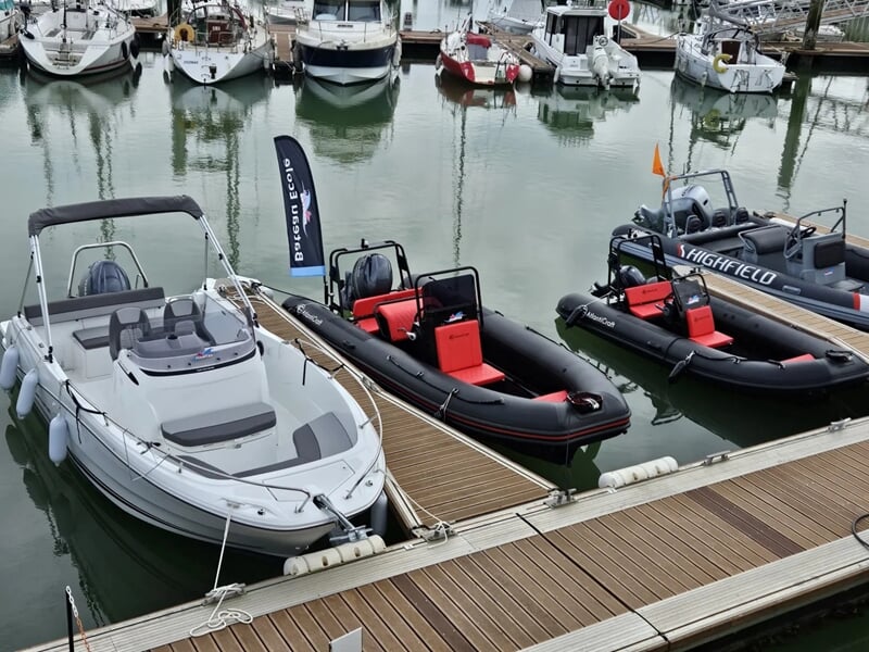 Bateau blanc et trois semi-rigides noirs amarrés à un quai en bois dans un port.