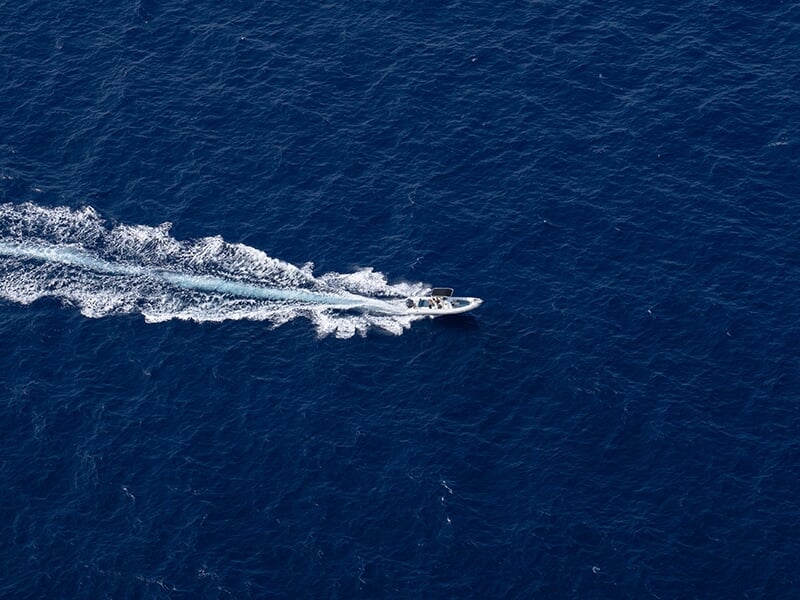 Vue aérienne d'un bateau à moteur naviguant à grande vitesse sur une mer bleue intense, laissant une traînée blanche d'écume derrière lui.