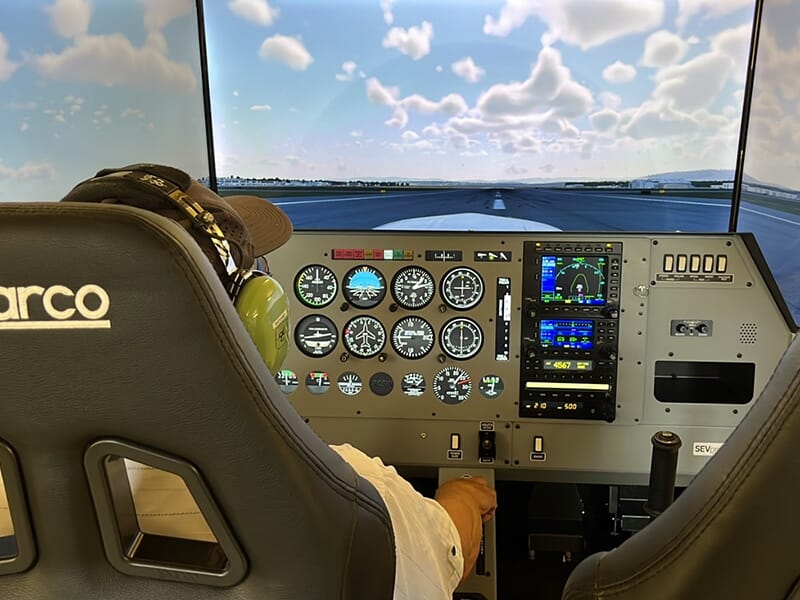 Cockpit d'un simulateur de vol avec des instruments détaillés, un pilote portant un casque.