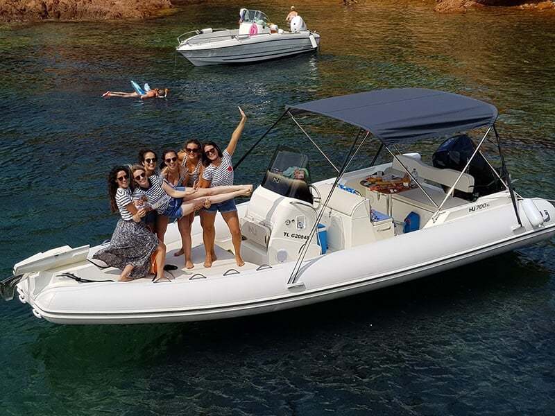 Groupe de personnes souriantes posant sur un bateau pneumatique blanc ancré dans une eau cristalline, d'autres embarcations visibles en arrière-plan