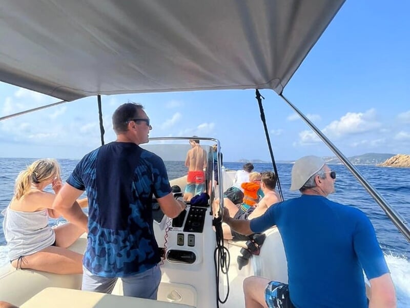 Groupe de personnes sur un bateau en mouvement, profitant de la vue sur la mer, sous un auvent pour se protéger du soleil.