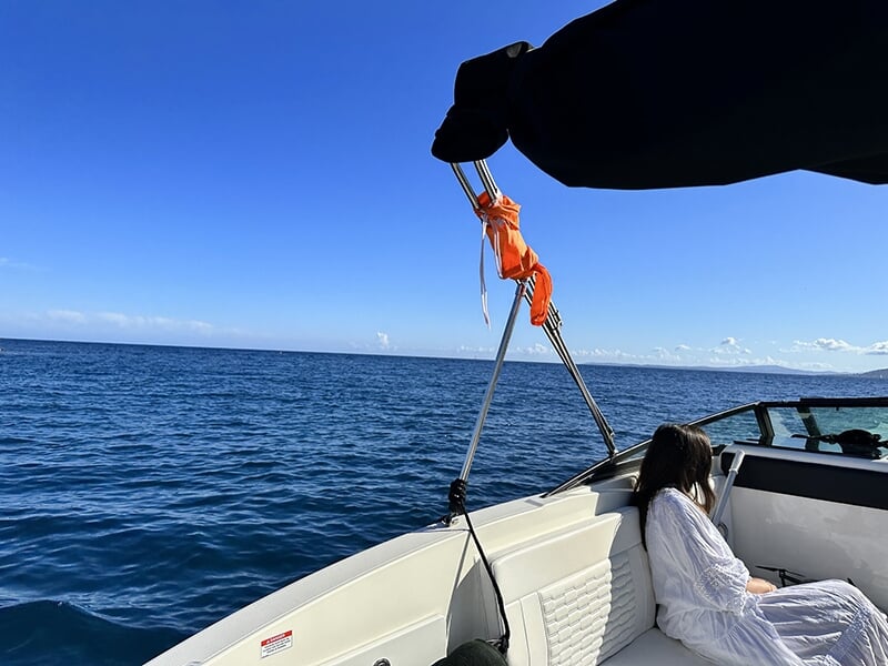 Personne assise sur l'arrière d'un bateau, regardant la mer ouverte sous un ciel bleu éclatant.