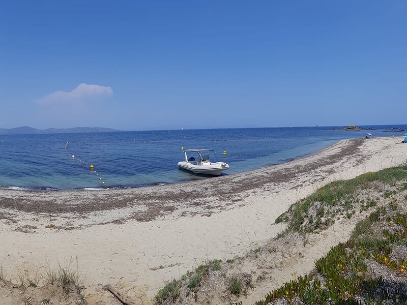 Petit bateau amarré sur une plage isolée avec sable blanc et mer turquoise, vue sur un paysage côtier calme.