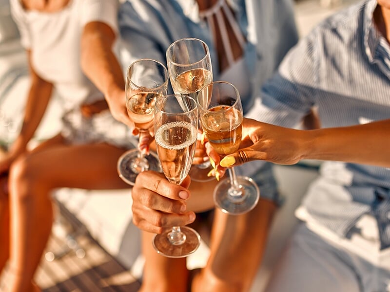 Gros plan sur des verres de champagne levés pour un toast, avec des gens souriants en arrière-plan sur un bateau.