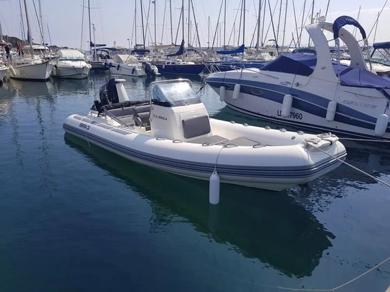 Un bateau semi-rigide blanc avec des rebords gonflables, amarré dans un port entouré d'autres bateaux et voiliers.
