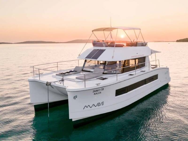 Catamaran blanc au coucher du soleil sur une mer calme, avec panneaux solaires sur le toit et paysage lointain, lors d'une croisière à Saint-Tropez.