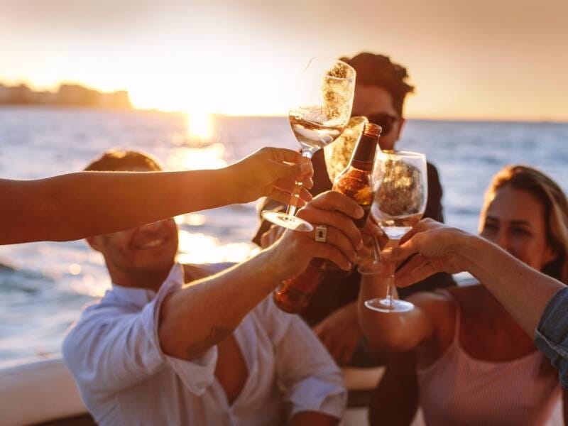 Groupe d'amis trinquant avec des verres et une bouteille sur un bateau au coucher du soleil en mer Méditerranée.
