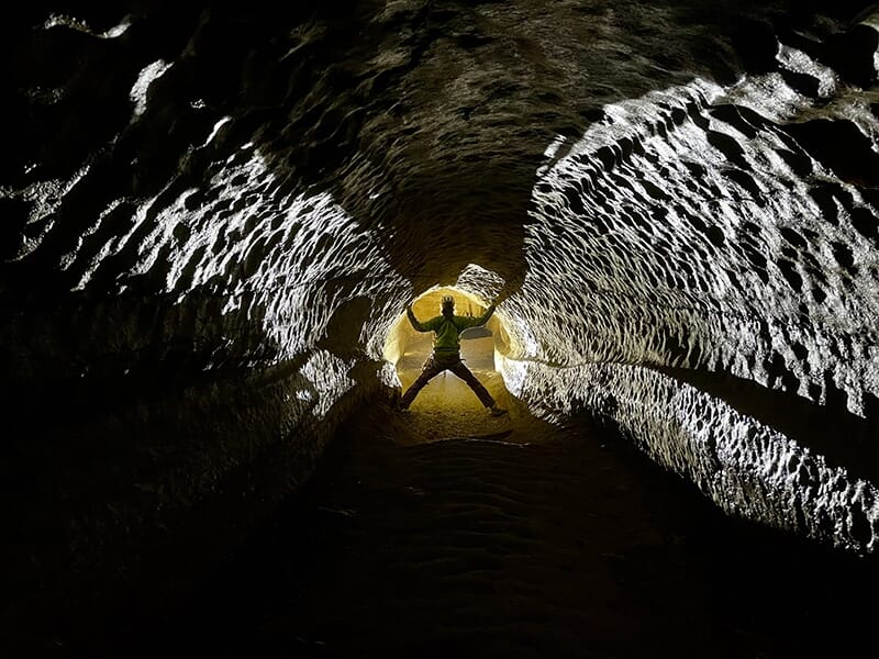 Un explorateur dans un tunnel souterrain éclairé de manière spectaculaire, adoptant une posture en étoile contre les parois.