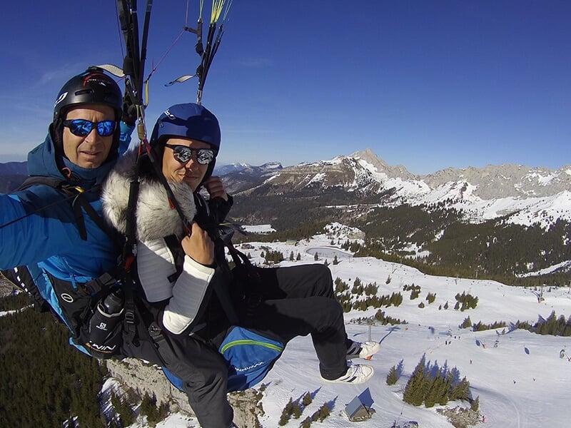Deux personnes en parapente capturent un selfie en plein vol au-dessus d'un paysage hivernal spectaculaire.