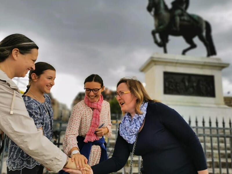 Quatre femmes rient et posent la main au centre en signe d’unité devant la statue équestre d’Henri IV sur l’île de la Cité.