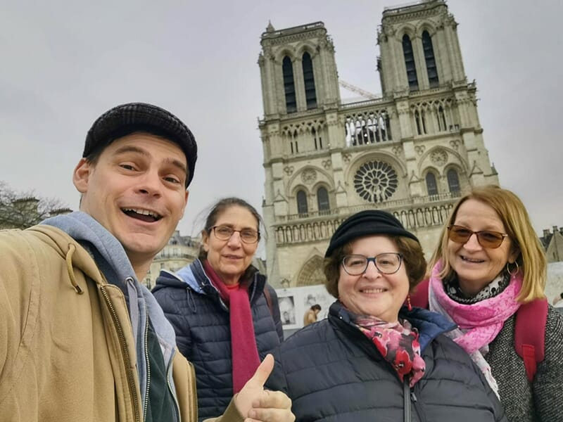 Un petit groupe de personnes souriantes pose pour une photo devant la cathédrale Notre-Dame de Paris.