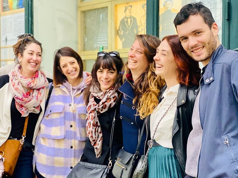 Groupe de six personnes souriantes, posant devant une vitrine avec des affiches anciennes.