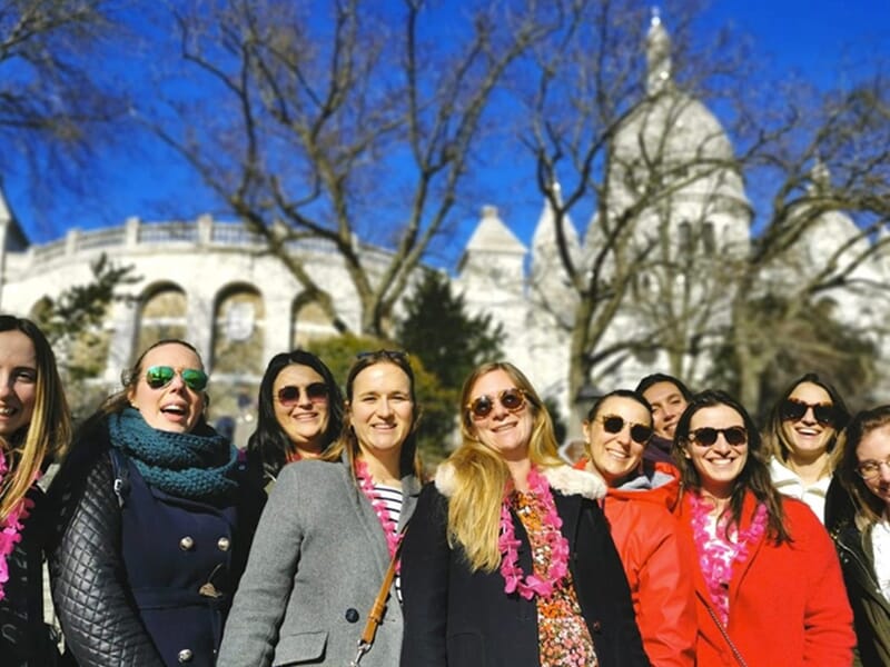 Groupe de femmes souriantes posant devant la basilique du Sacré-Cœur par une journée ensoleillée.
