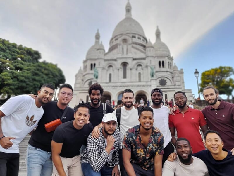 Groupe d’amis posant devant le Sacré-Cœur, tous souriants, par une journée claire.
