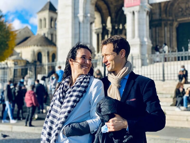 Un couple complice se regarde en souriant devant le Sacré-Cœur, en arrière-plan flouté.