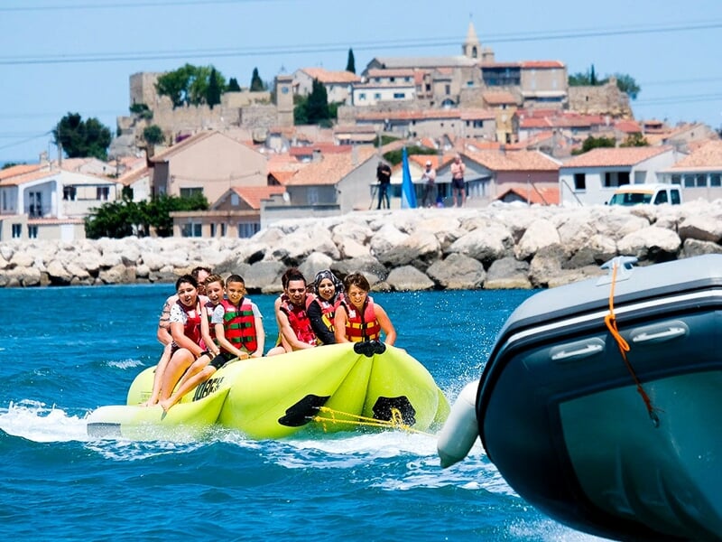 Un groupe de personne sur une bouée tractée par un bateau avec un village en arrière plan