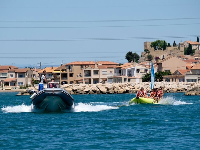 Bateau tractant une bouée avec un groupe sur la mer et ville en fond 