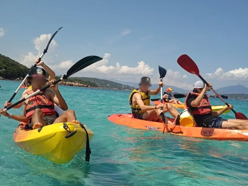 Un groupe de jeunes pratiquant le kayak sur une eau turquoise avec la côte en fond